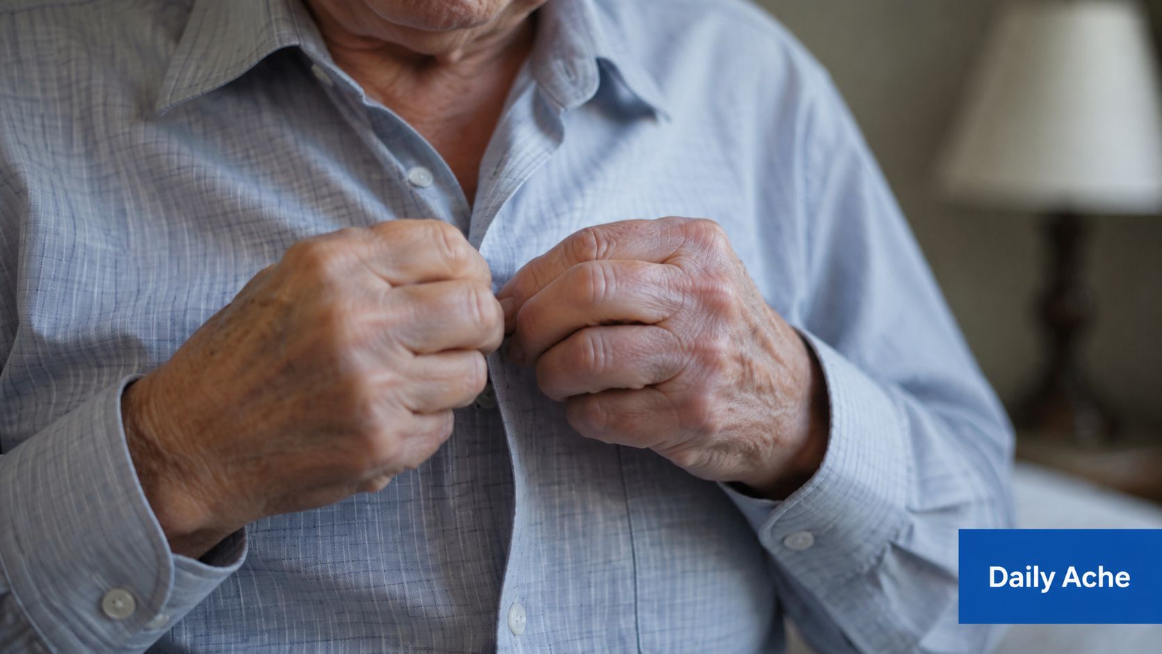 Close up of an elderly person struggling to button their light blue shirt due to hand pain.
