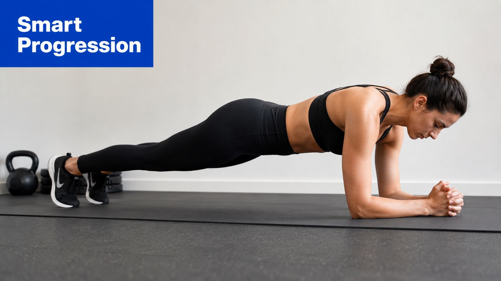 A fit woman performing a forearm plank exercise on a black yoga mat in a gym setting.
